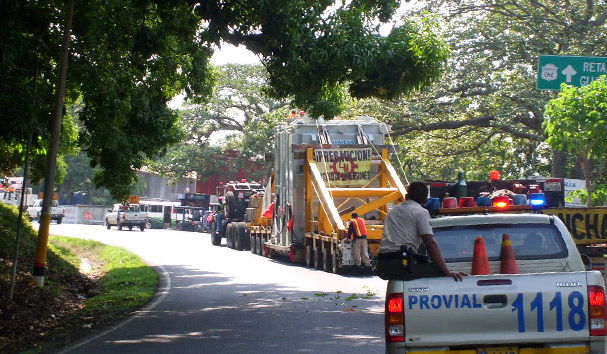 Tráiler con carga sobredimensionada escoltado por vehículos de seguridad. Transporte de maquinaria pesada en Guatemala.
